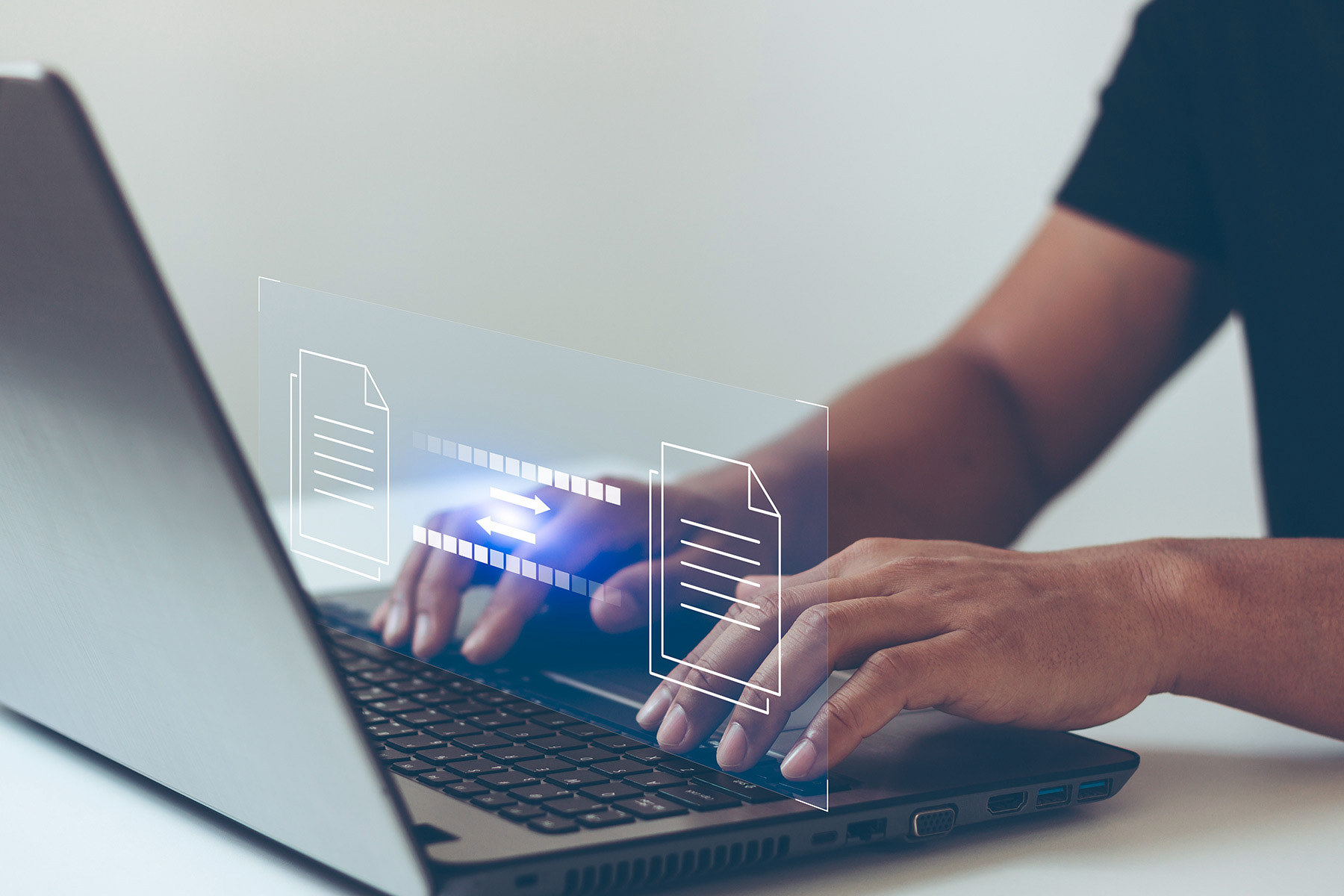 A person types on a laptop keyboard. Above the keyboard, two document icons are shown with an arrow pointing from the left to the right, symbolizing file transfer or data sharing.
